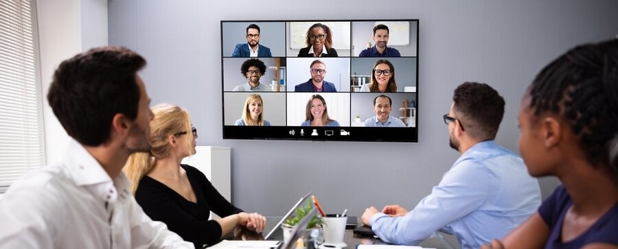 A meeting with in-office employees and remote staff utilizing conference room technology to communicate.