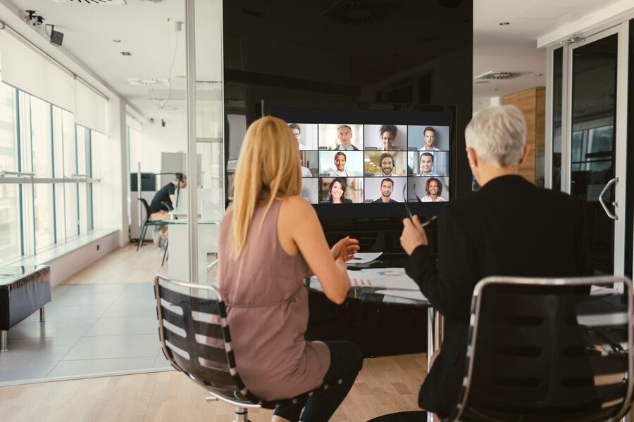 A group of employees on a video conference call in the middle of an office space.