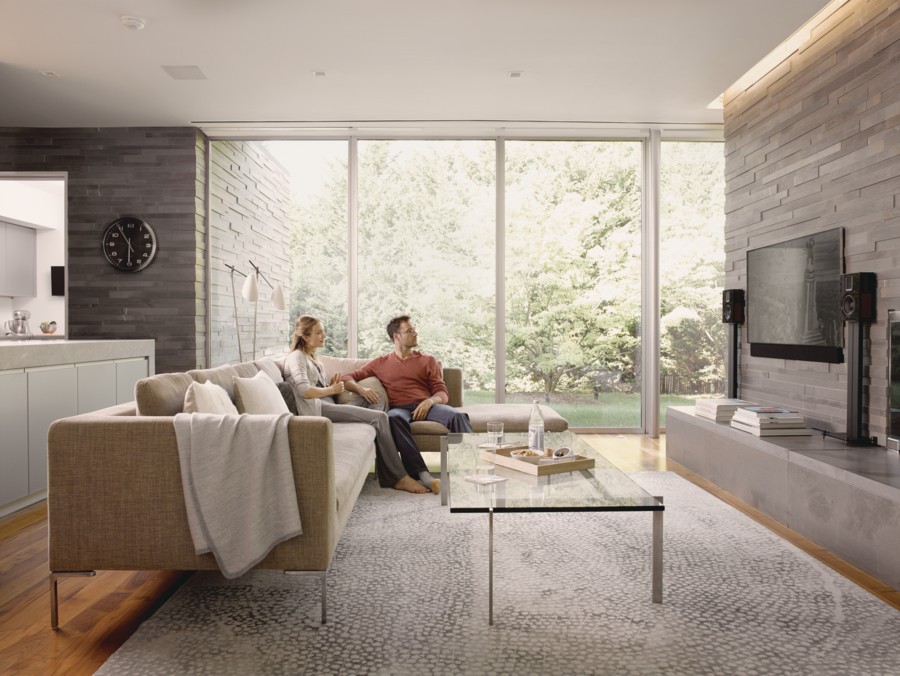 A man and a woman watch television in a spacious living room with lots of natural light.