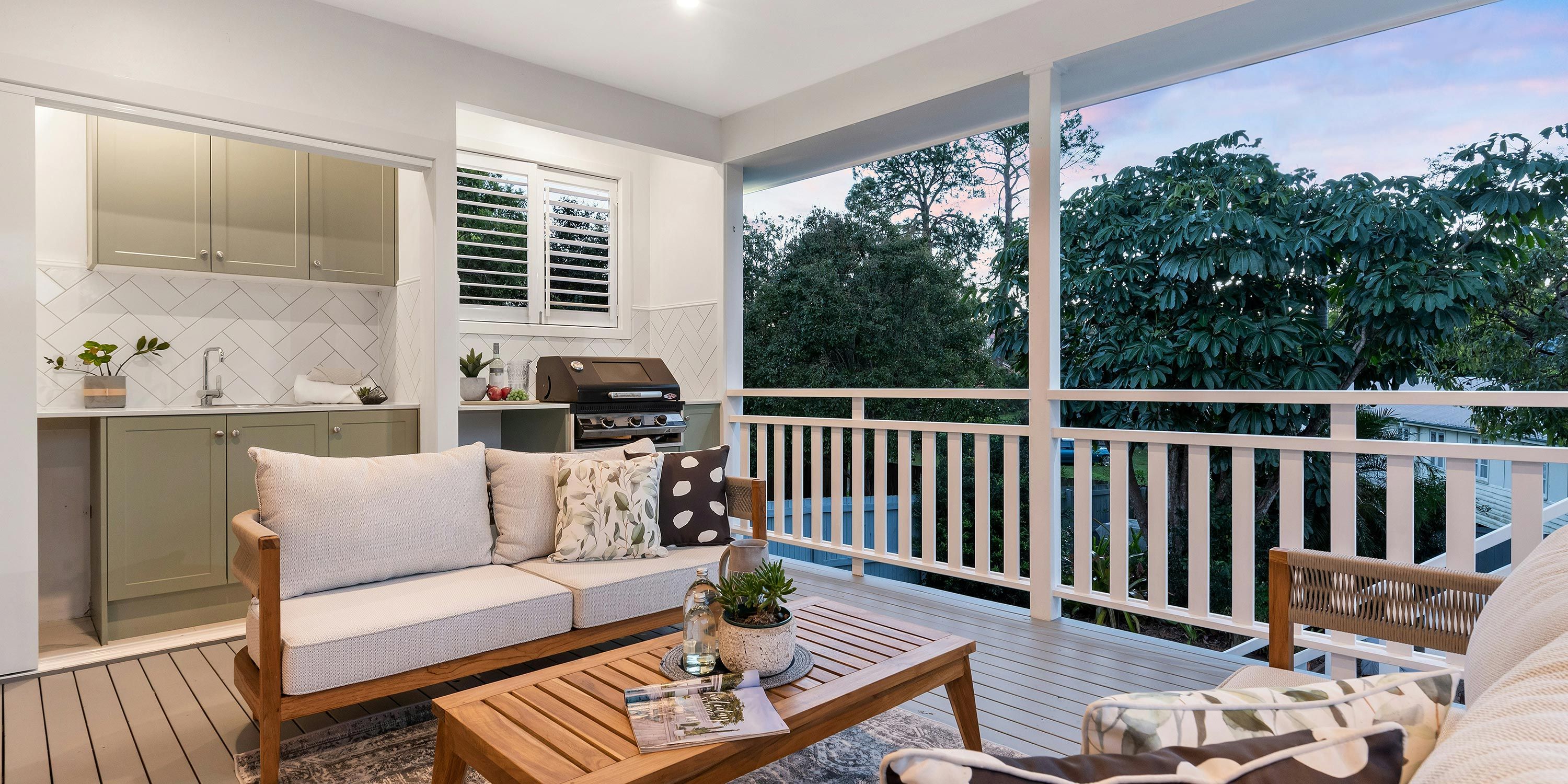 An inviting outdoor kitchen with light green cabinets, a grill, and a cozy seating area on a wooden deck surrounded by nature.