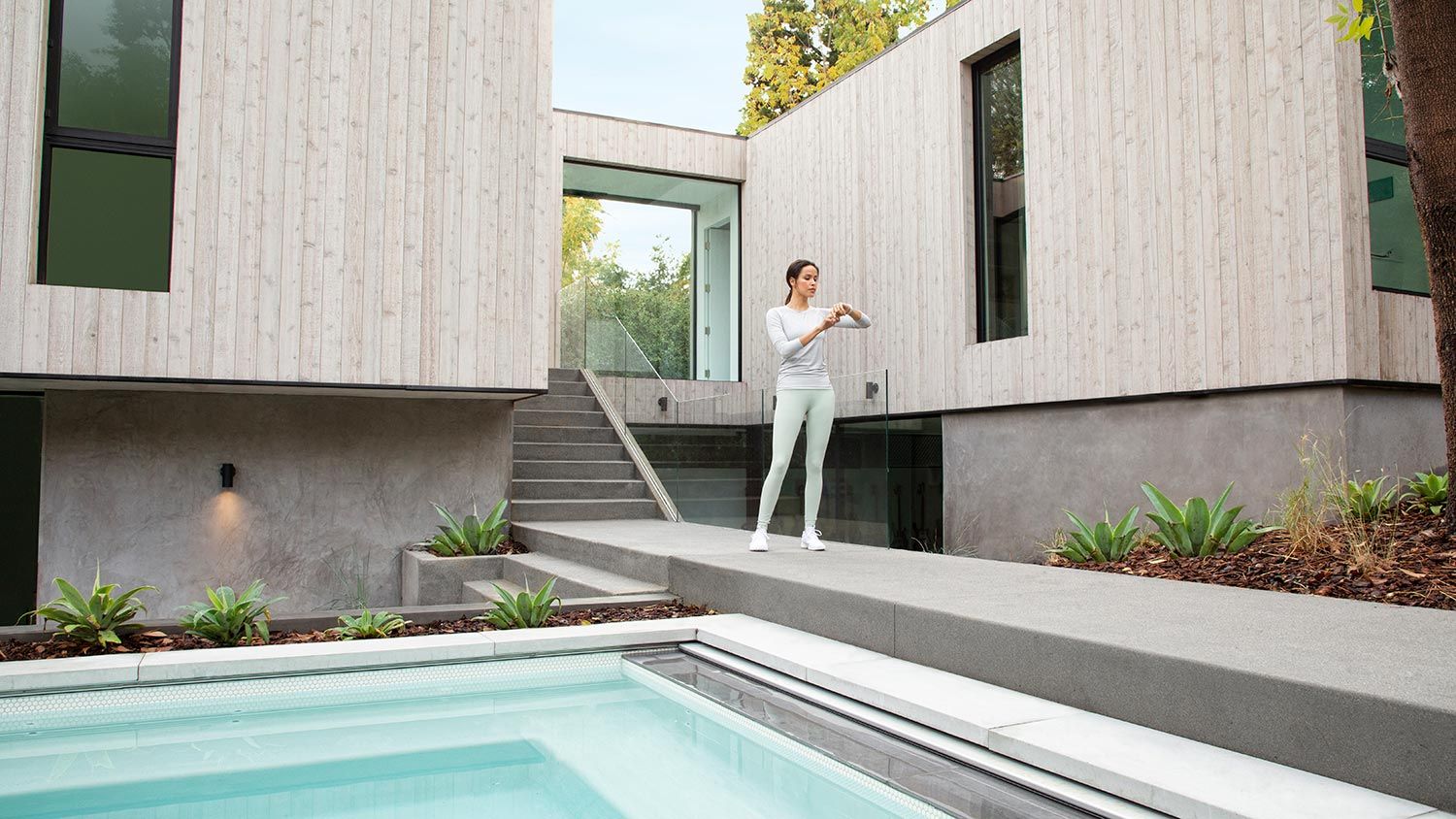 A woman controls her pool settings using a Savant interface on her Apple Watch, enjoying seamless smart home integration.